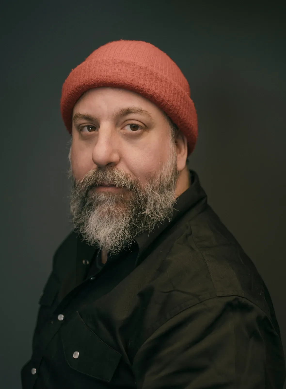 Pablo Saravanja in a red knit toque and a dark shirt, looking toward the camera against a dark backdrop.